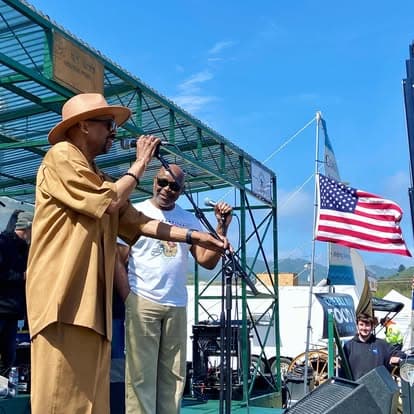 Person wearing a sun hat and sunglasses enjoying live music at Pacific Coast Dream Machines festival in Half Moon Bay, California