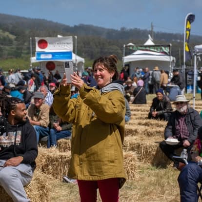 Smiling woman in a stylish hat enjoying live music at Pacific Coast Dream Machines event in Half Moon Bay, California.