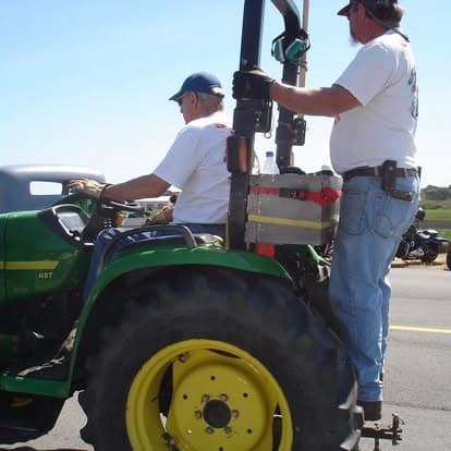Vintage blue tractor with a worker in denim overalls and cap at Pacific Coast Dream Machines event, Half Moon Bay.
